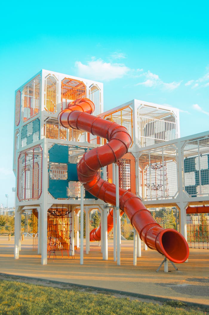 A vibrant playground with a red spiral slide on a sunny day.